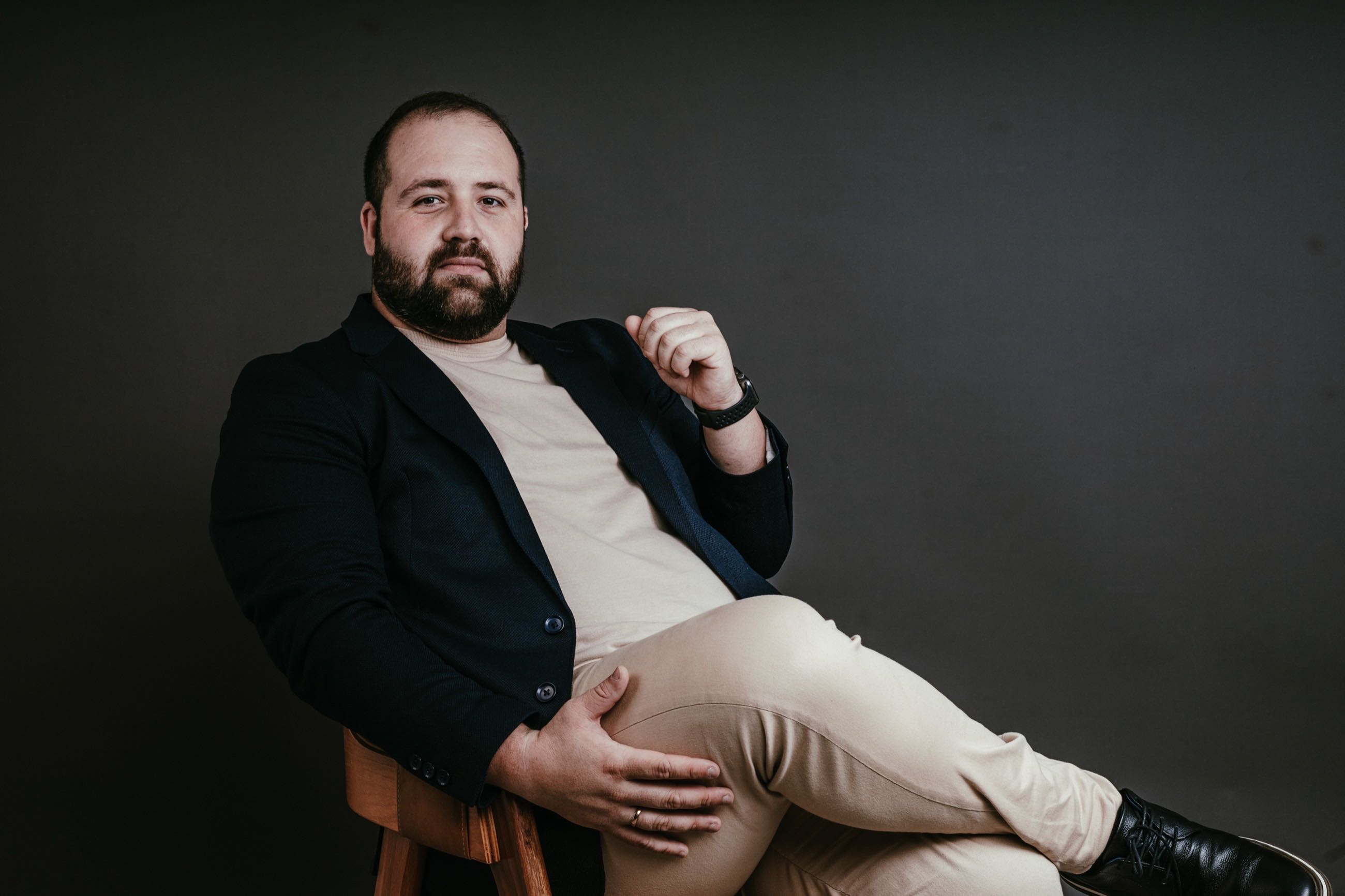 Homem de blazer escuro recostado numa poltrona, fundo cinza
